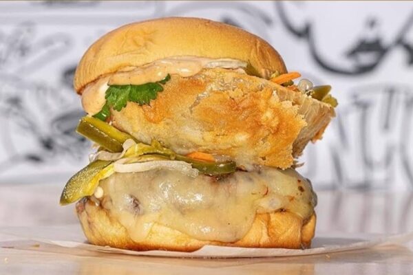 Close-up of a gourmet craft burger with melted cheese, jalapeños, and fresh cilantro, served on a toasted bun